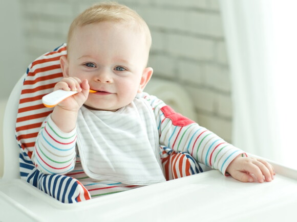 Baby zufüttern-Lachendes Baby mit Löffel  